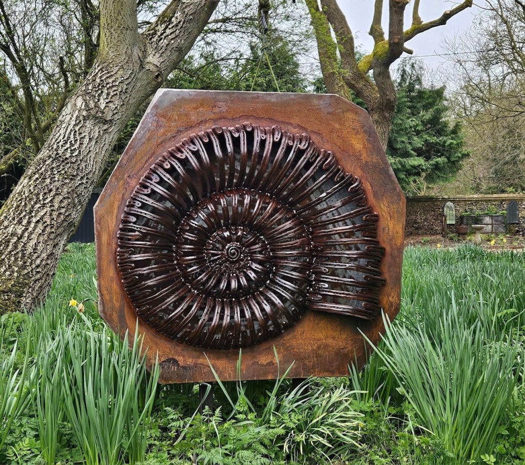 Ammonite metal sculpture in wooded area